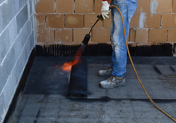 Worker preparing part of bitumen roofing felt roll 